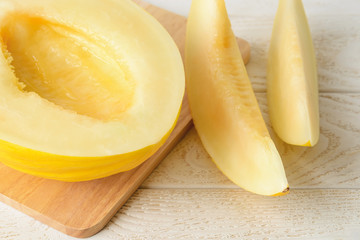 Half and two slices of ripe juicy honeydew melon on a brown cutting board over withe wood table. Sweet fruits and berries. Vegetarian, raw food diet and healthy eating.