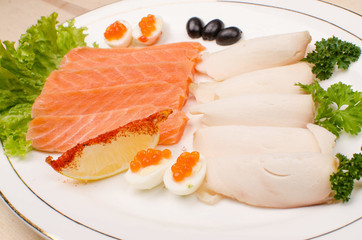 on a white plate is a salmon fillet sliced and chicken fillet surrounded by greens with lemon