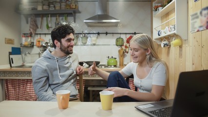 Young happy couple talking during breakfast in the kitchen