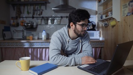 Fototapeta na wymiar Happy young businessman working on laptop in kitchen at home at night