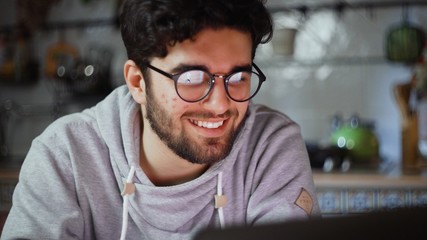 Obraz premium Close up of happy man working on laptop in kitchen at home at night