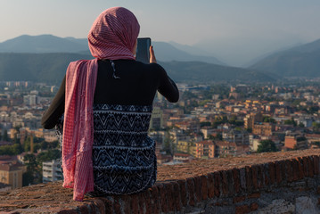 Egyptian woman with smartphon on the roof terrace with aerial view of the old Italian city Brescia.