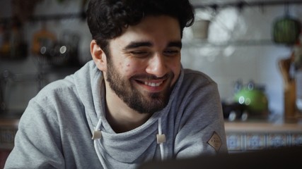 Obraz premium Close up of happy man working on laptop in kitchen at home at night