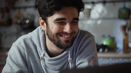 Close up of happy man working on laptop in kitchen at home at night