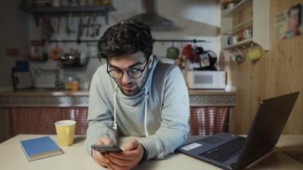 Young happy man using smartphone in kitchen at home at night