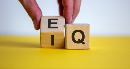 Hand flips a cube and changes the expression 'IQ' to 'EQ'. Beautiful yellow table, white background. Concept of emotional and  intelligence quotient. Copy space. - obrazy, fototapety, plakaty
