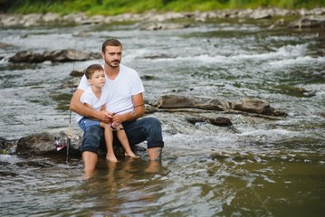 A father teaching his son how to fish on a river outside in summer sunshine. father's day.