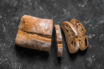 Ciabatta. Dark fresh healthy flattish open-textured Italian bread with a floury crust made with olive oil on black rustic background. Close-up. Top view