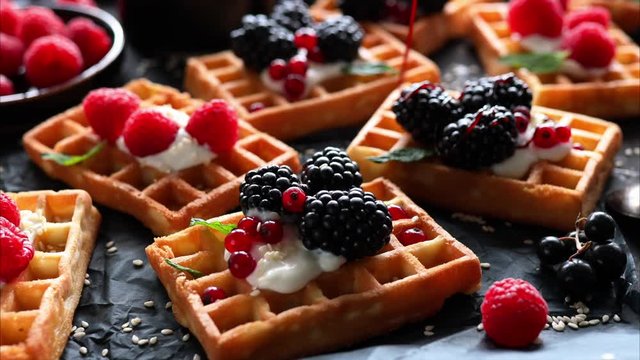 Pouring molasses on waffles with fresh berries close-up view