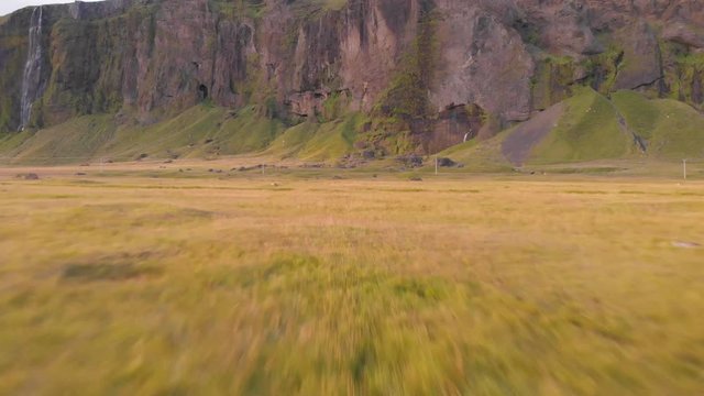 Aerial footage flying very close to the ground over the grass. The images are close to a huge cliff with beautiful waterfalls.