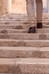 Fototapeta na wymiar Legs of modern person in beige trousers who is walking up by the stairs. Light warm colours, vertical photo