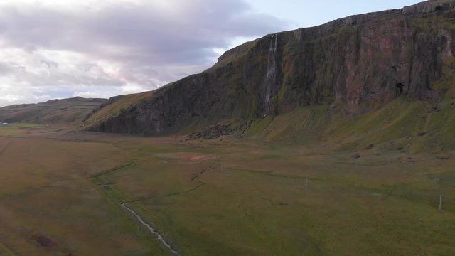 Aerial images moving away from a cliff full of beautiful waterfalls and surrounded by green meadows. Typical Icelandic landscape.