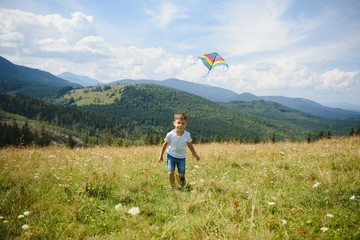little boy holds string of kite flying in blue sky with clouds in summer with copyspace