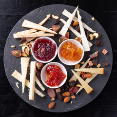 Cheese board with nuts and marmalades on a black slate background - gastronomy - gourmet
