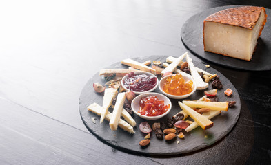 Cheese board with nuts and marmalades on a black slate background - gastronomy - gourmet