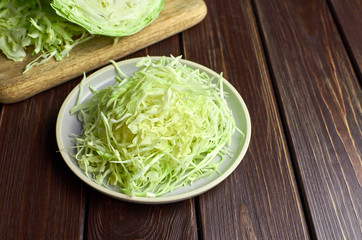Chopped fresh green cabbage salad on ceramic plate on wooden table background.