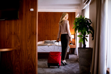 Young businesswoman arrives in a hotel room with red suitcase