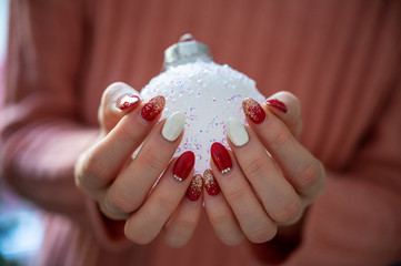 Female hands with stylish holiday manicure holding shiny white christmas bauble