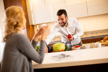 Woman drinking coffee at the kitchen table while man preparing food