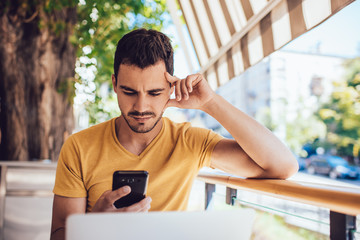Serious caucasian male blogger checking notifications on smartphone using 4G for chatting in social networks, pensive man freelancer confirming online payment via cellular banking application.
