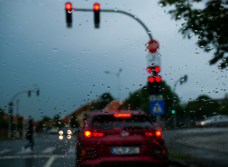 Rain drops on the windshield, cars waiting for the green light in the blured background at sunset...