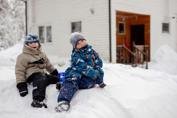5-6 year old boys sitting on snow slide on winter day. country house on backgrownd