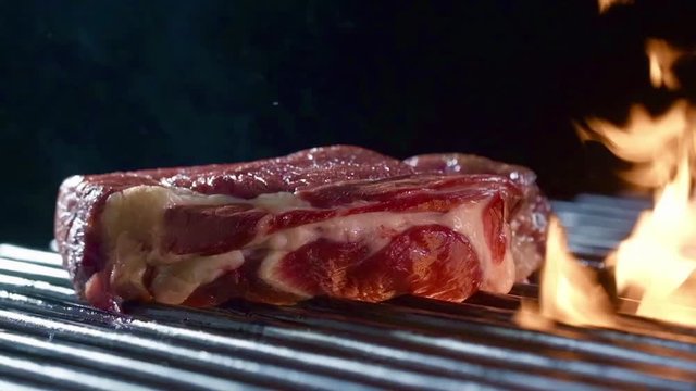 Raw beef steak falls on grill with burning fire and smoke.