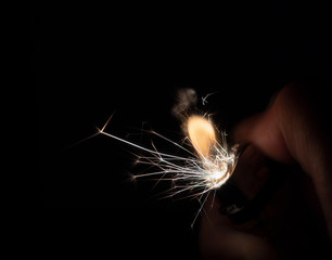 Flame and sparks fly from lighter hold by hand in dark environment with black background