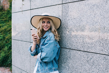 Delighted lady with smartphone leaning on building wall