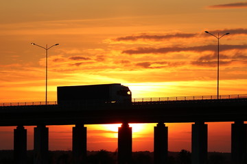 A truck driving on a flyover at sunset - obrazy, fototapety, plakaty