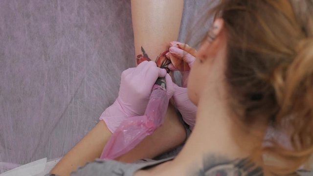 A close-up view of a professional woman tattooist who is tattooing on the leg of a young girl. The view from the top.