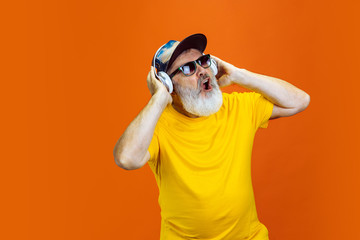 Fototapeta premium Crazy dance. Portrait of senior hipster man using devices, gadgets isolated on orange studio background. Tech and joyful elderly lifestyle concept. Trendy colors, forever youth. Copyspace for your ad.