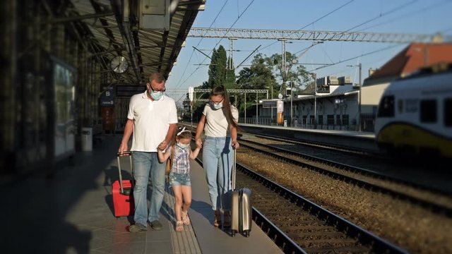 Family with a girl 5-6 years old and suitcases is walking along the platform. There are medical masks on the faces of passengers. Travel, tourism during the COVID-19 epidemic.