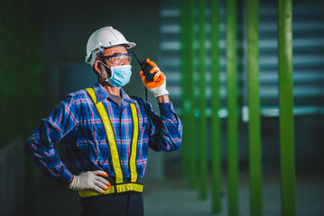 Elderly male engineers and construction workers wear masks to prevent the coronavirus (COVID-19) during work and use radio communication.