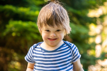 Portrait of baby boy with Down syndrome playing in summer day on nature