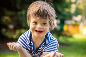 Portrait of baby boy with Down syndrome playing in summer day on nature