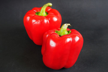 close-up of two large juicy red peppers on a black background side view . red vegetables