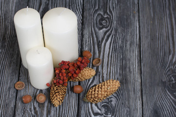 Three white candles stand on painted pine planks. Nearby are spruce cones, dried rowan berries and acorns.