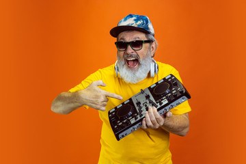 DJ-set. Portrait of senior hipster man using devices, gadgets isolated on orange studio background. Tech and joyful elderly lifestyle concept. Trendy colors, forever youth. Copyspace for your ad.