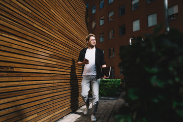 Cheerful freelancer with smartphone walking in street