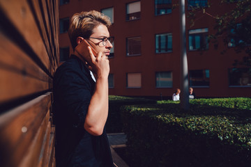 Fototapeta premium Serious student answering phone call near wooden building