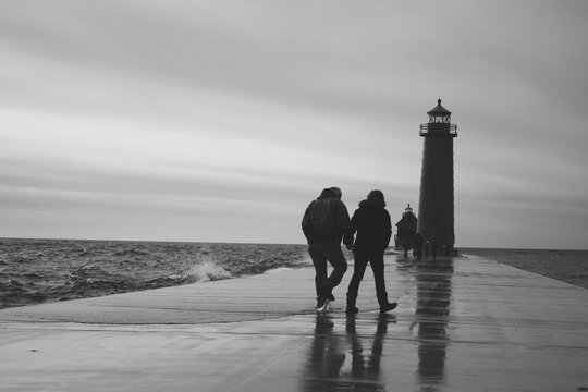 Balck and white photo of people walking on a pier towards a lighthouse.