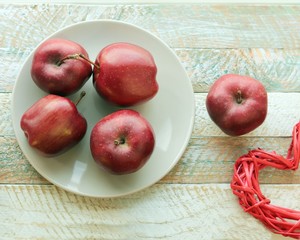 Red fresh apples on a plate, bright cloth on a wooden table, healthy food concept, organic fruits, autumn season, at home