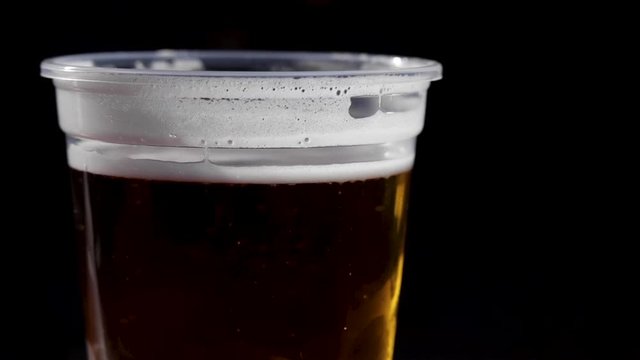 Close up pint of beer in plastic cup with bubbles rising, black background