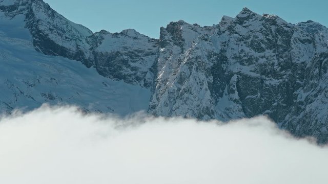 Snow capped mountains above clouds in a blue sky in sunny weather