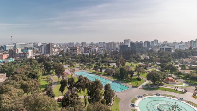 Aerial view to Park of the Reserve with magic water circuit biggest fountain complex timelapse. Green lawn and trees. City skyline on a background