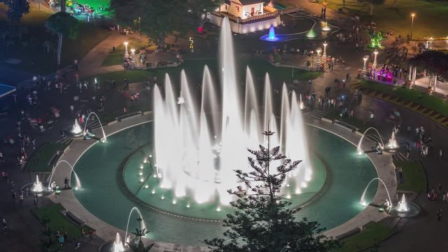 Aerial view to Park of the Reserve with colorful magic water circuit biggest fountain complex illuminated at night timelapse. Green lawn and trees.