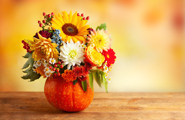 Autumn bouquet of beautiful flowers and berries in a pumpkin on wooden  table. Concept of autumn festive decoration for Thanksgiving day.