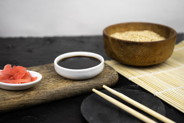 Japanese kitchen background with bamboo mat, chopsticks, soy sauce, pickled ginger and brown rice