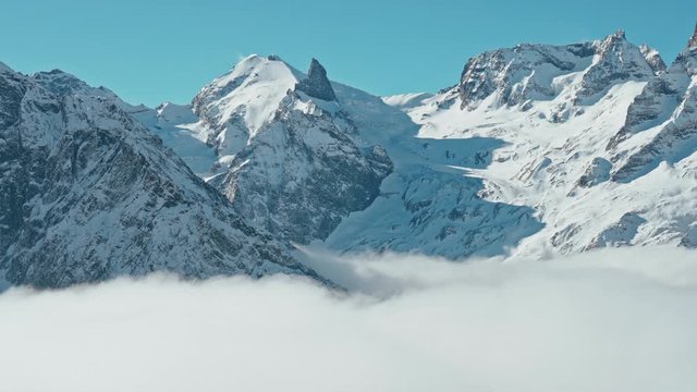 Snow capped mountains above clouds in a blue sky in sunny weather